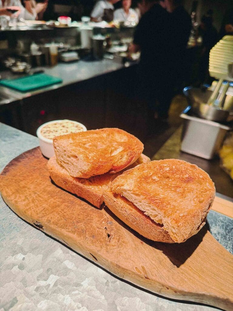 Toasted sourdough bread slices served on a wooden board with a side of Kombu Butter from Lolla Singapore.