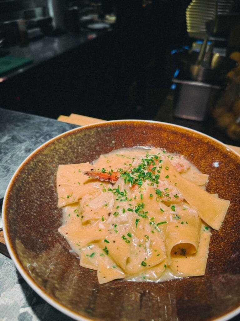 Hand-torn pappardelle pasta in a creamy sauce with brown crab meat, garnished with chives from Lolla Singapore.