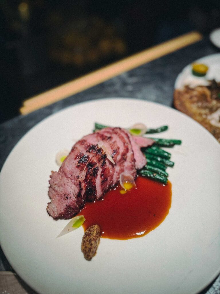 Sliced, medium-rare Grilled Iberico Pork Collar served with green beans and a rich red wine jus from Lolla Singapore.