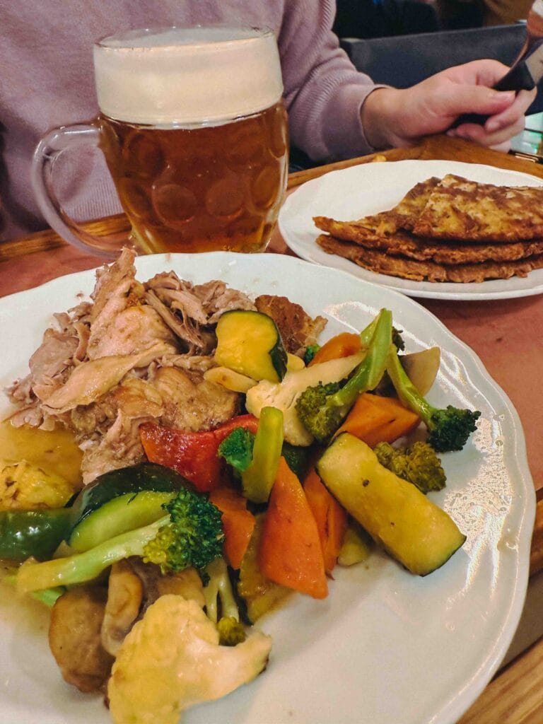 A tray of assorted roasted Czech meats and seasonal vegetables served with a crispy garlic potato pancake (bramborák).