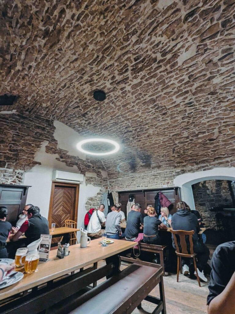 Rustic, vaulted dining room of the traditional U Glaubiců Prague medieval cellar restaurant, with an exposed stone ceiling and patrons sitting at long wooden tables.