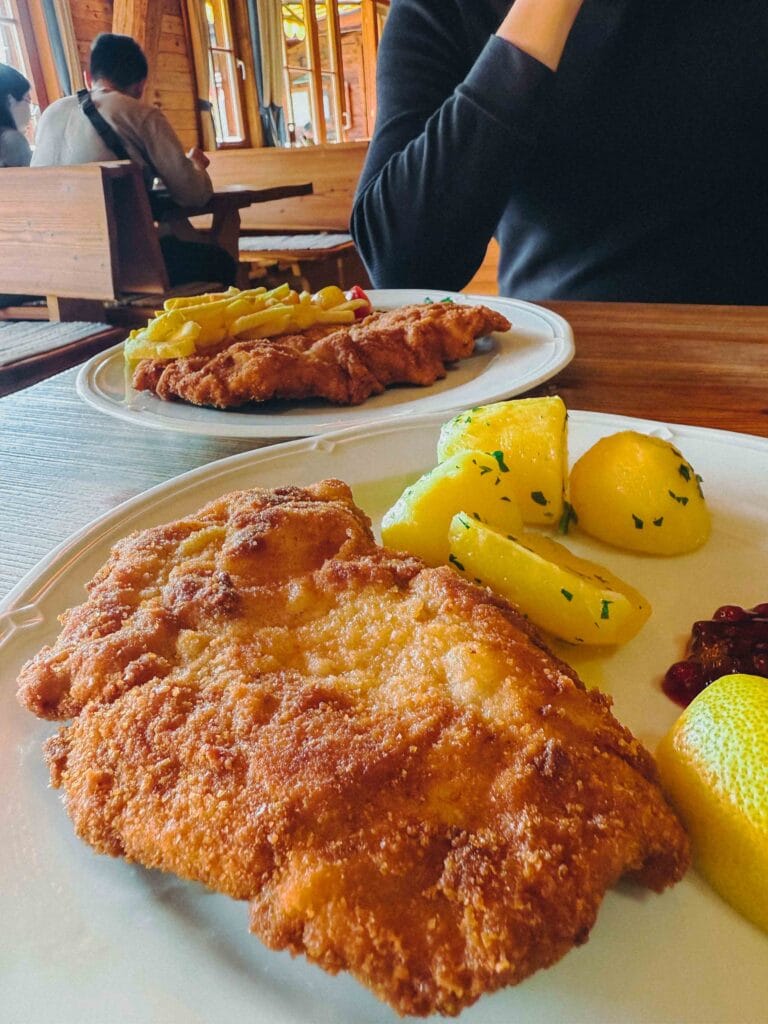 A large, crispy breaded pork schnitzel served with a lemon wedge and parsley garnish on a white plate at Dorf-Alm.