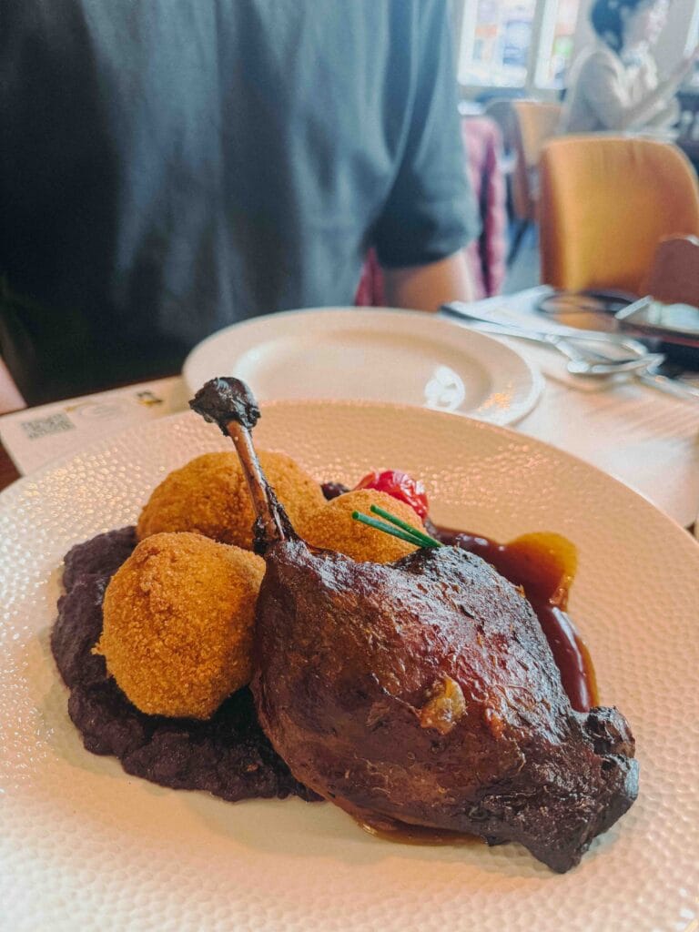 A tender duck confit leg served with a golden-brown alpine cheese croquette and a smooth, bright purple cabbage puree.