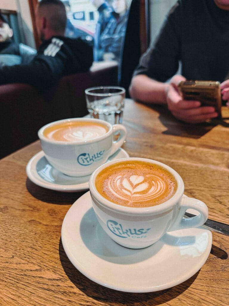 Two white ceramic cups of coffee with latte art on a wooden table at Cirkusz Café.