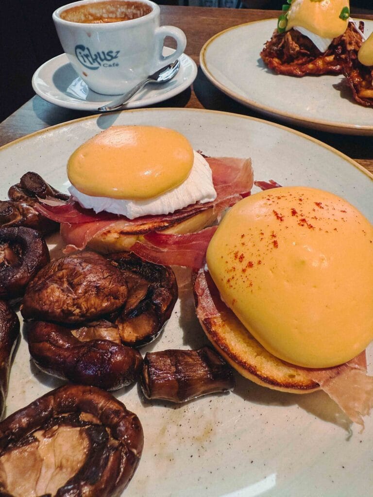 Eggs Benedict served with thin slices of Jamón Ibérico and a side of large sautéed mushrooms.