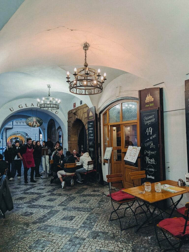 Outdoor seating under a vaulted, covered cobblestone passage in Prague's Malá Strana, with the entrance to the historic U Glaubiců Prague medieval cellar restaurant.