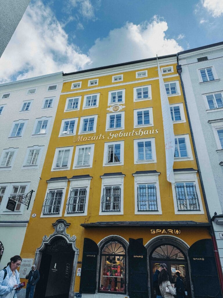 The bright yellow facade of Mozarts Geburtshaus (Mozart's Birthplace) in Salzburg's Getreidegasse street, featuring white-framed windows and a small SPAR store on the ground floor.