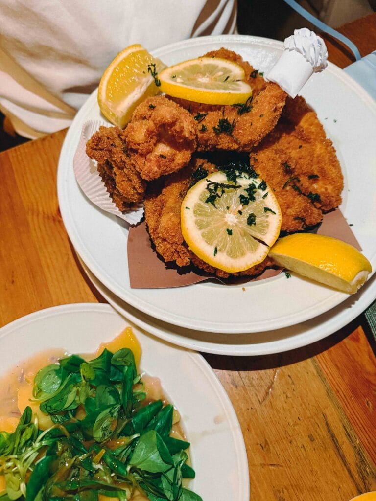A generous serving of crispy, deep-fried chicken pieces (Backhendl) served on a white plate with a side of traditional Viennese potato salad.