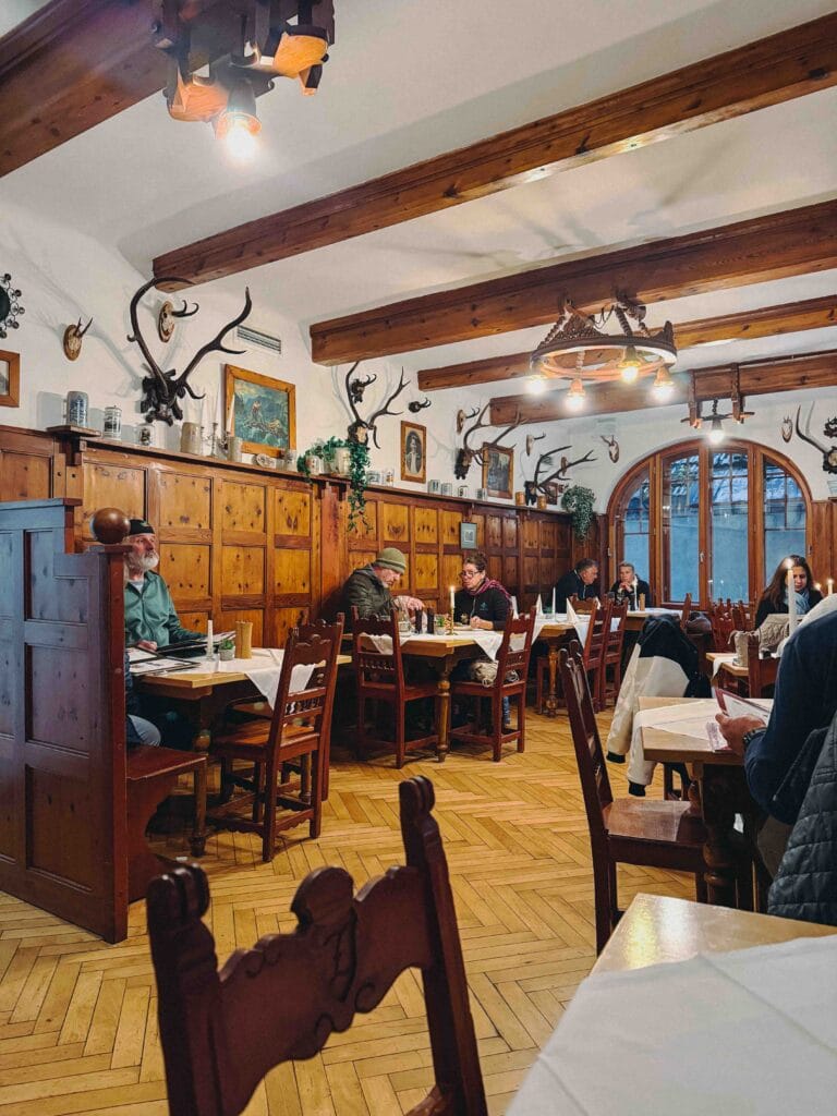 The traditional, wood-paneled interior of the Seewirt Zauner restaurant in Hallstatt, featuring rustic hunting decor (antlers) and patrons seated at wooden tables for a meal.