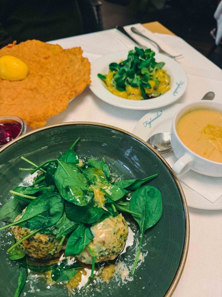 Two large green spinach dumplings (Spinatknödel) drizzled with melted brown butter and topped with freshly shaved parmesan cheese.
