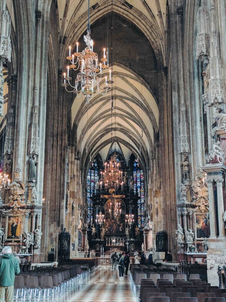 The vast, vaulted interior of St. Stephen's Cathedral, showing the nave, high Gothic arches, historic chandeliers, and stained glass windows.