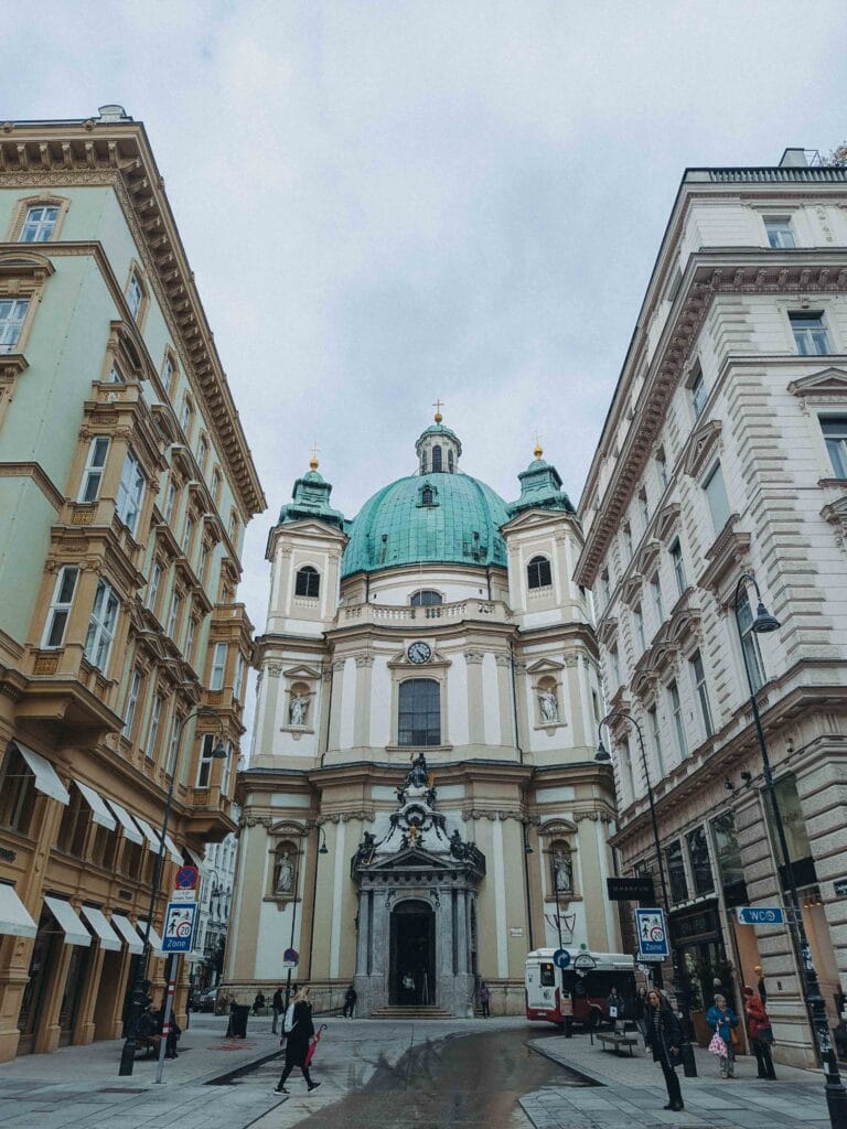 The impressive Baroque facade and copper dome of St. Peter's Church (Peterskirche), framed tightly by the narrow street and surrounding traditional Viennese buildings.