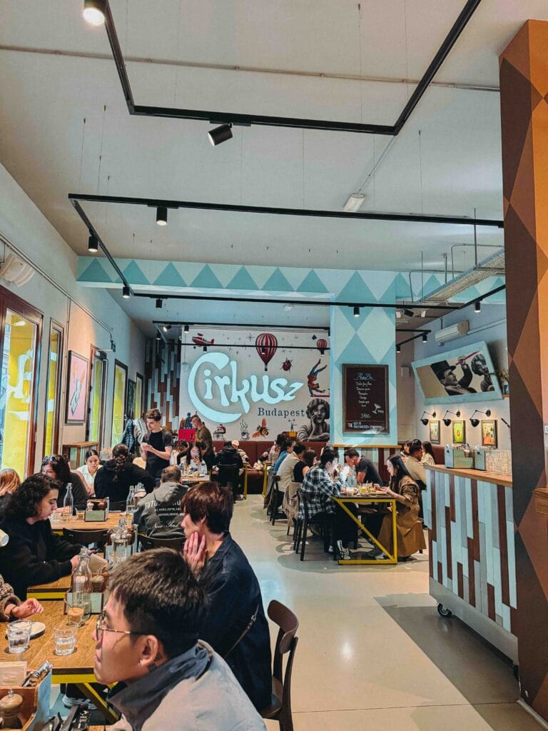 Vibrant interior of Cirkusz Café in Budapest with circus-themed wall art and busy diners.