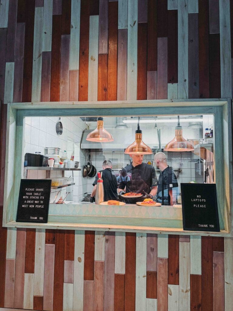 Open kitchen at Cirkusz Café with chefs preparing food and "No Laptops" signs on the counter.
