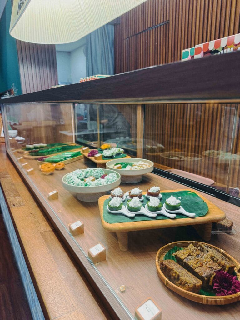 Glass display counter of colourful kuih and banana cake on banana leaves at Nenek Johor Bahru