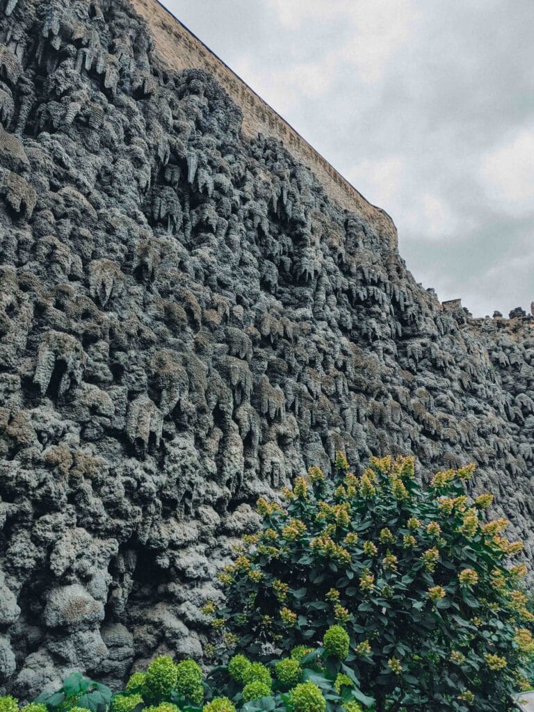 The unusual, artificial grey Grotto Wall made of stalactite-like stucco, with green shrubs at the base, in Wallenstein Palace Gardens, Prague.