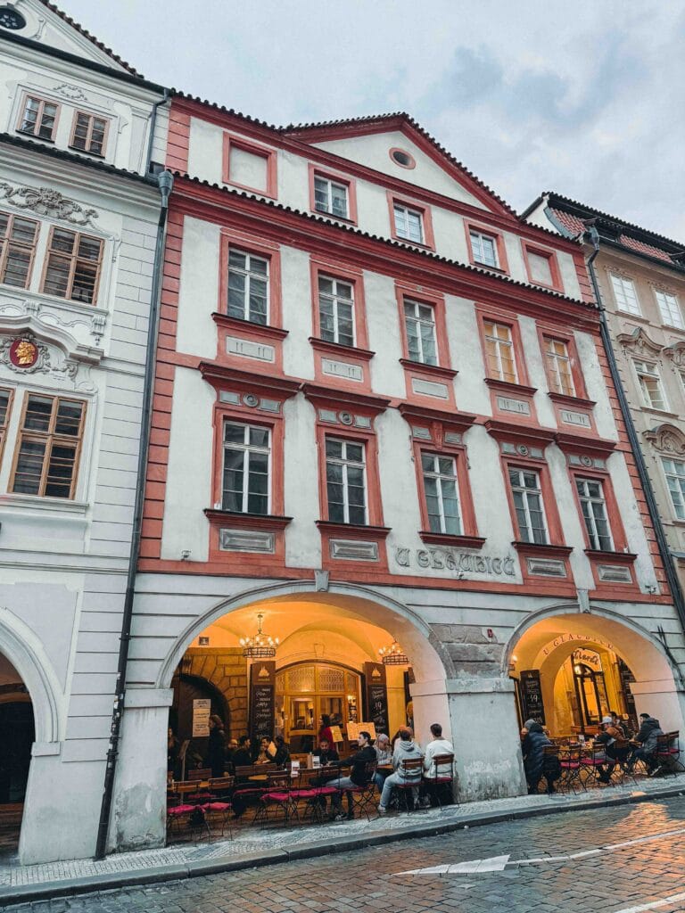 The charming, historic street-level facade of U Glaubiců pub in Prague, showing the small, arched entrance and traditional signage against a cobblestone street.