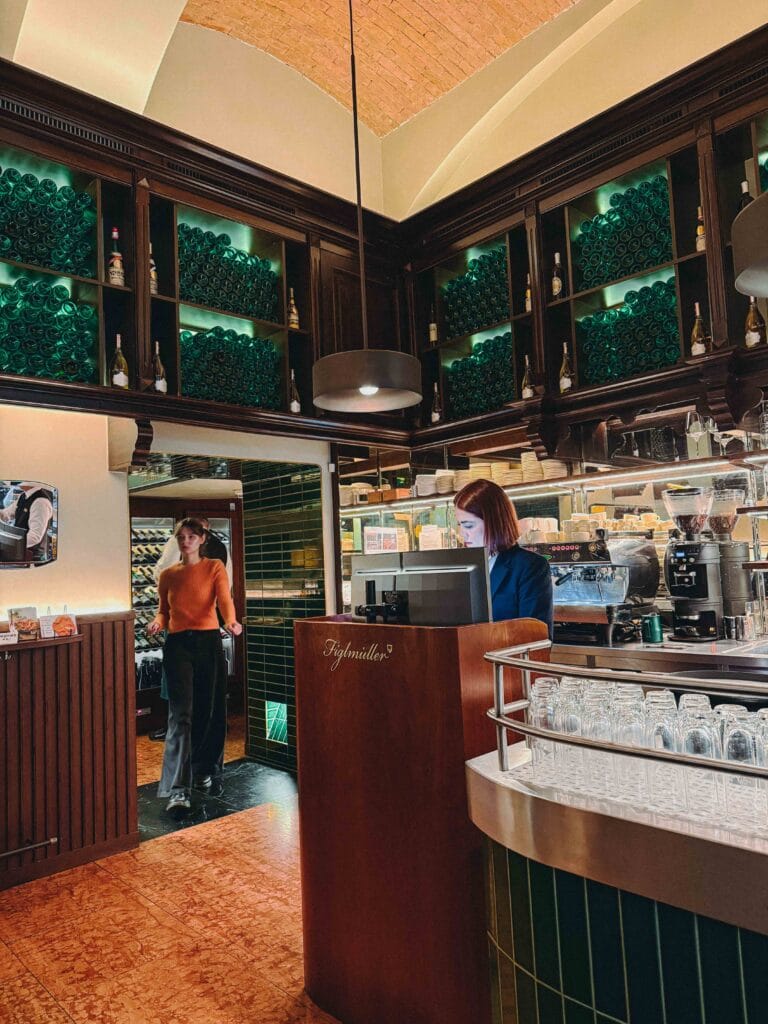 The rustic, traditional interior of Figlmüller restaurant in Vienna, showing wood-paneled walls, wooden chairs, and guests seated at tables under warm lighting.