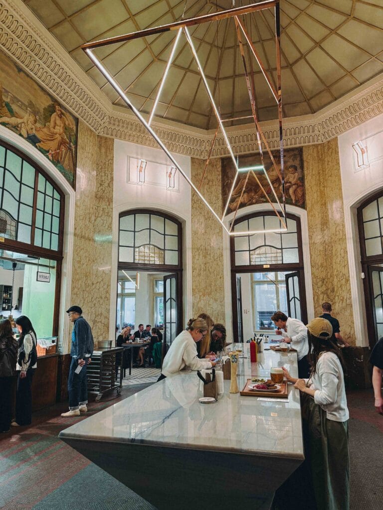 The high-ceilinged, industrial-style dining hall of Kantýna in Prague, featuring stone walls and communal tables.