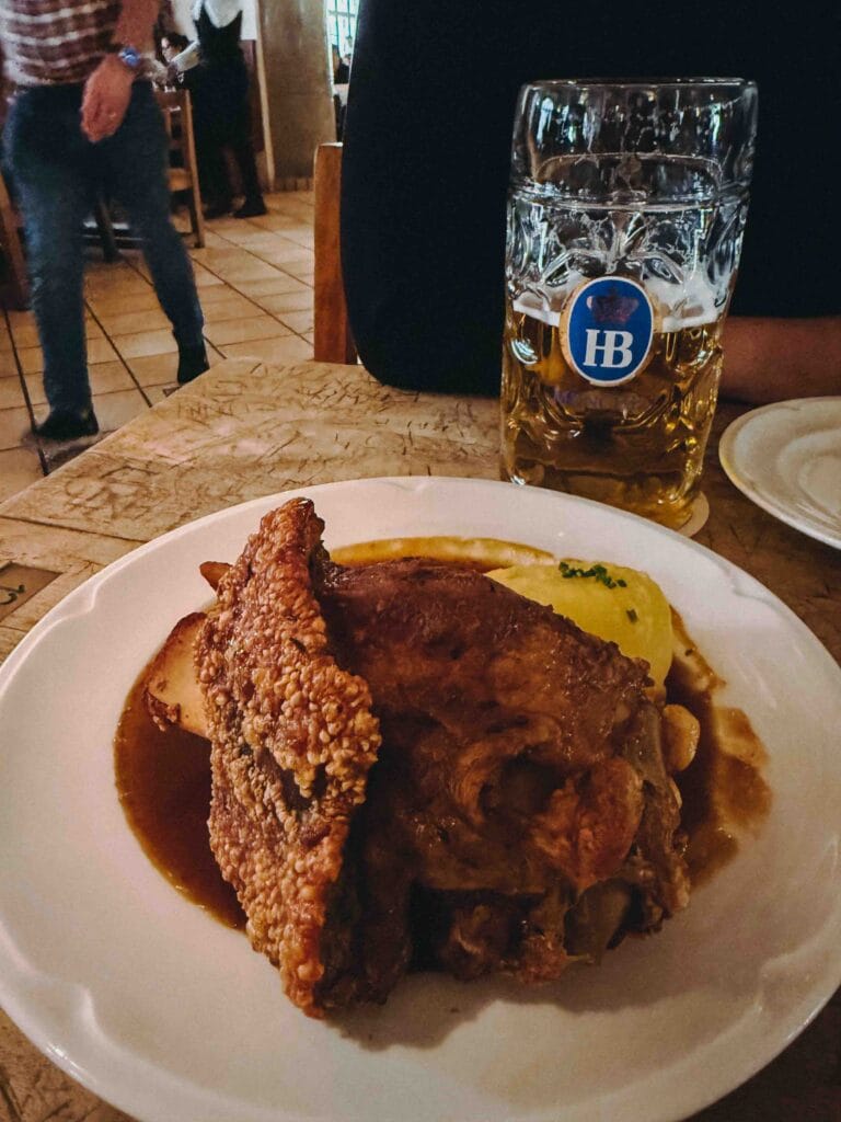 Crispy Pork Knuckle with dark beer sauce and a potato dumpling next to a liter of Hofbräu beer.
