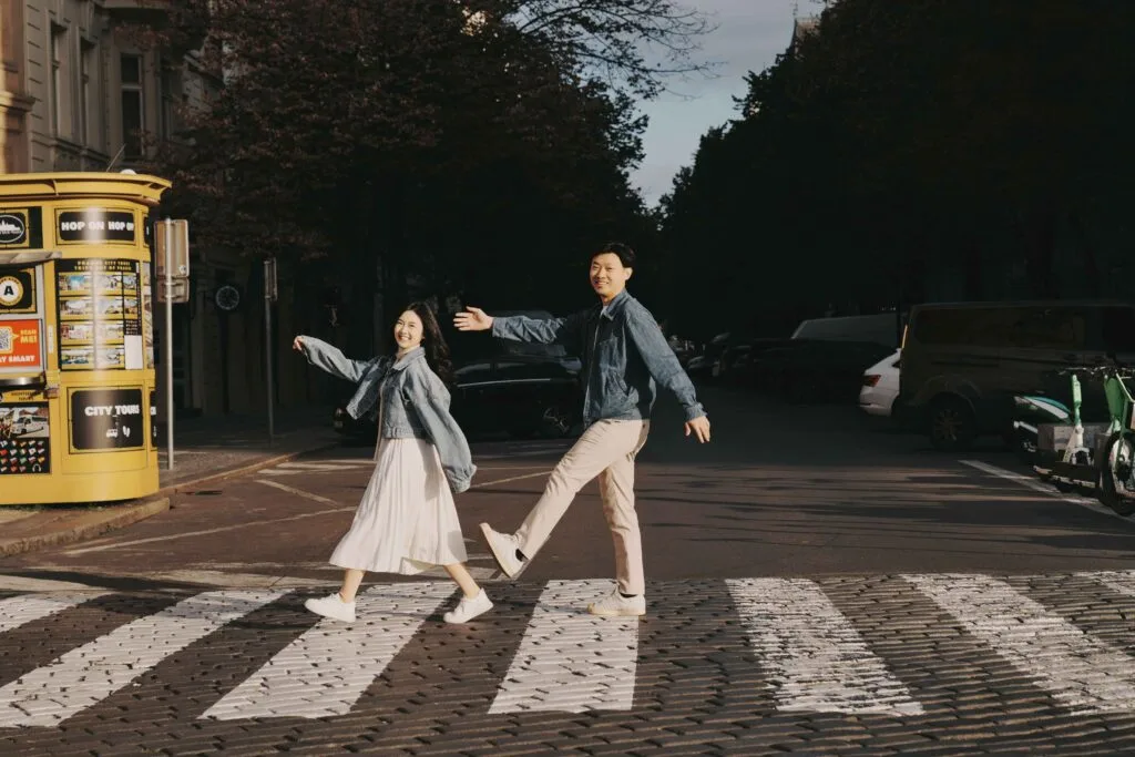 Li Yang and Valerie joyfully crossing a cobblestone street in Prague with a Hop-On Hop-Off tour kiosk in the background