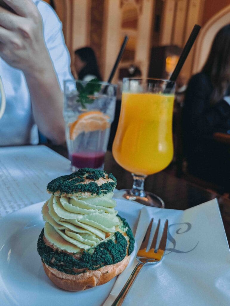 A close-up of a small French choux pastry (profiterole) dusted with sugar and filled with green pistachio cream, served on a white plate.