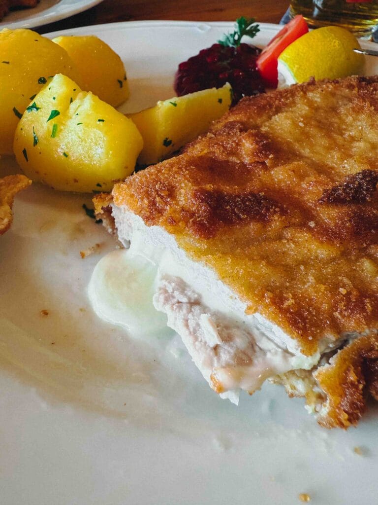 A golden-brown breaded Pork Cordon Bleu stuffed with ham and cheese, served with a lemon wedge at Dorf-Alm zu St. Wolfgang.