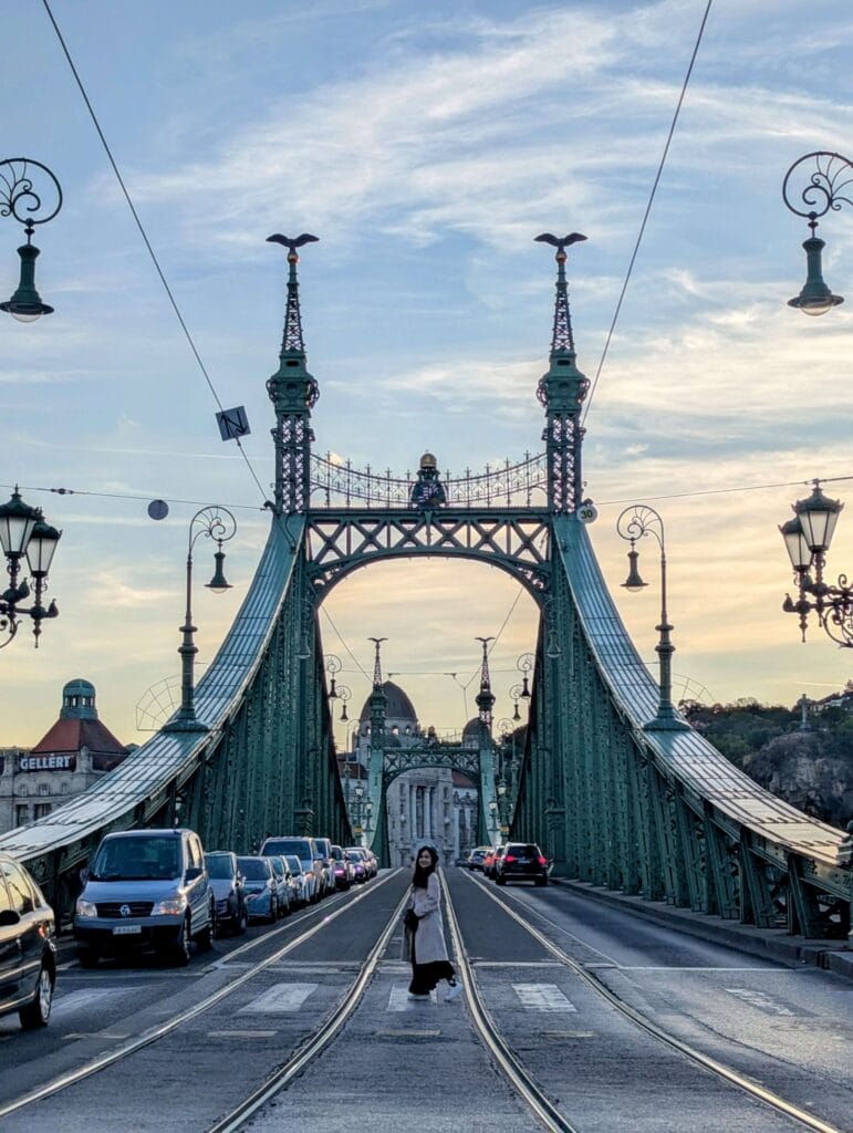 A stunning view of the Art Nouveau green steel Liberty Bridge connecting Buda and Pest across the Danube River, with its decorative Turul bird statues illuminated against the twilight sky.