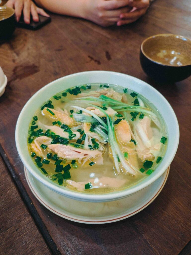 Bowl of Vietnamese chicken noodle soup with clear broth, poached chicken slices and spring onions at Cơm Linh Hội An