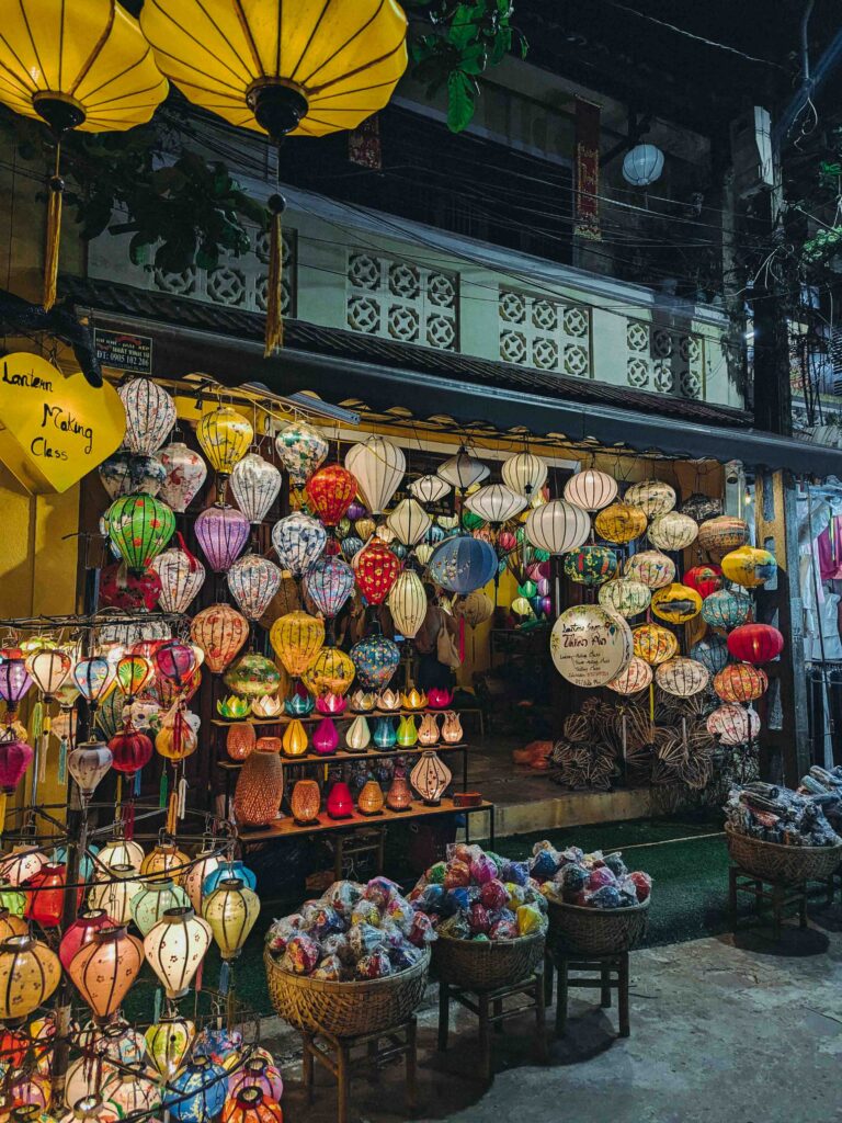 Hoi An Old Town lantern shop at night covered in colourful silk lanterns of all shapes and sizes with lantern making class sign