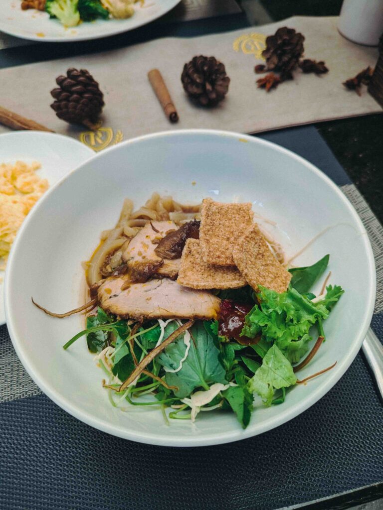 Bowl of Cao Lầu noodles with roasted pork crispy crackling and fresh herbs served at hotel breakfast at Royal Mansion Boutique Hotel Hoi An