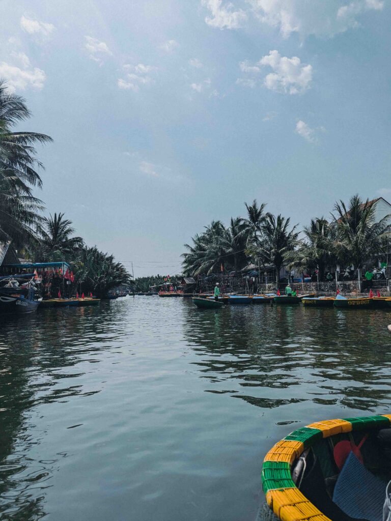 View from inside a coconut basket boat along a calm canal lined with coconut palm trees near Hoi An with basket boats moored on the banks