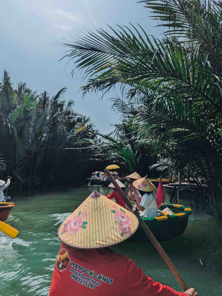 Hang Coconut Basket Boat tour boatwoman in conical hat paddling through narrow waterway in water coconut palm forest near Hoi An