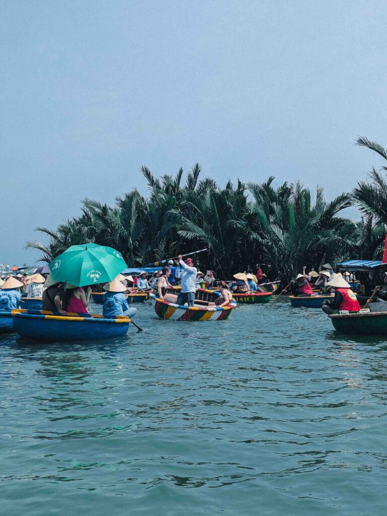 Multiple colourful coconut basket boats with tourists and boatmen in conical hats on open water near Hoi An coconut palm forest