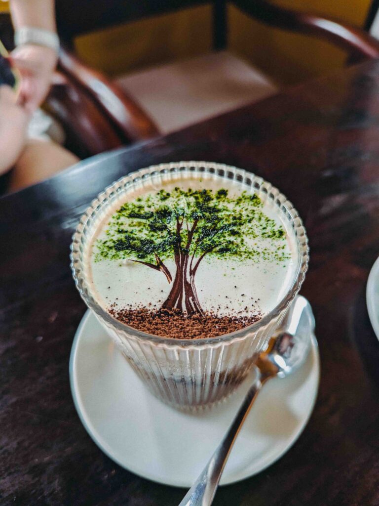 Vietnamese latte with intricate tree latte art in matcha and chocolate powder served in a ribbed glass at Uncle Huan Bistro Hoi An