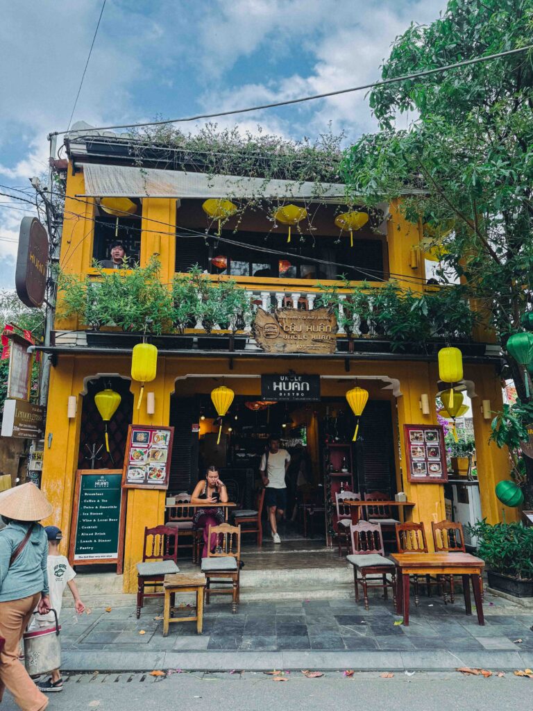 Uncle Huan Bistro exterior in Hoi An Old Town with yellow walls green and yellow silk lanterns and outdoor seating