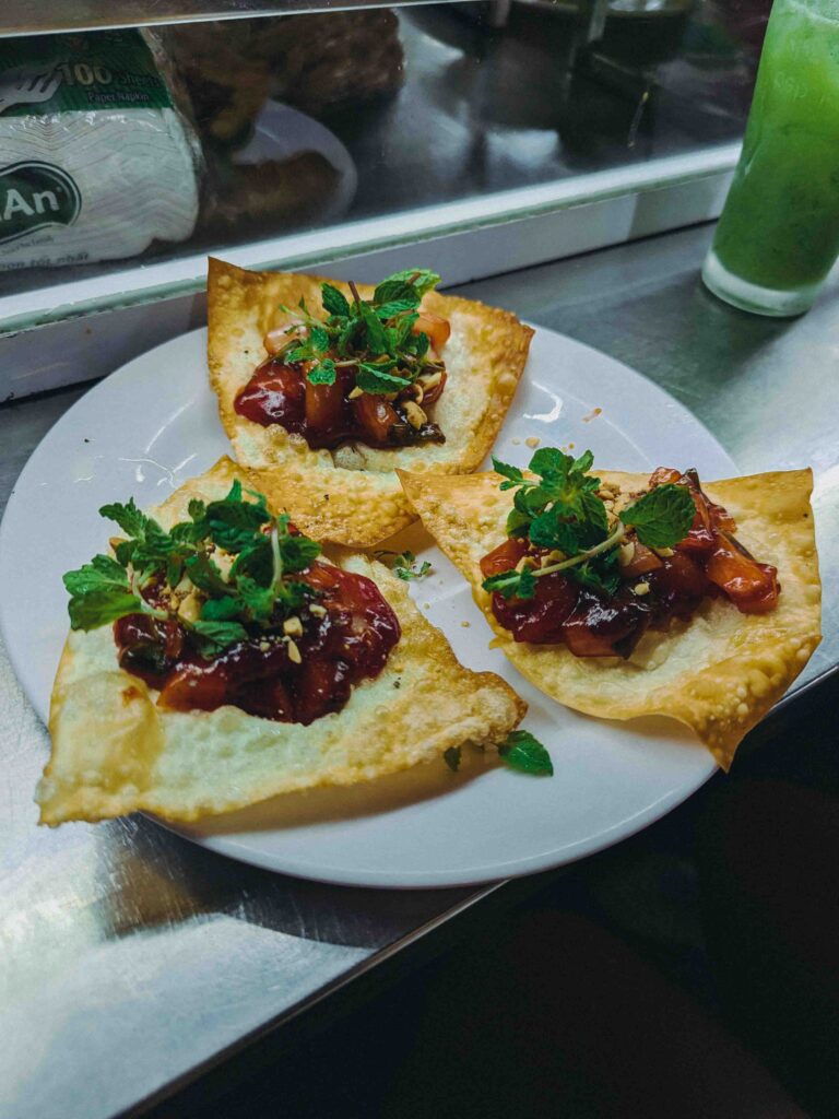 Three crispy wonton crackers topped with pork filling fresh mint and peanuts on a white plate at Hoi An Market