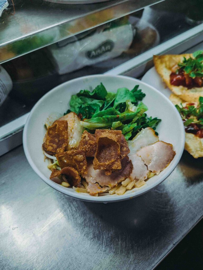 Bowl of Cao Lầu Hoi An noodles with roasted pork crispy crackling and fresh greens at Hoi An Market