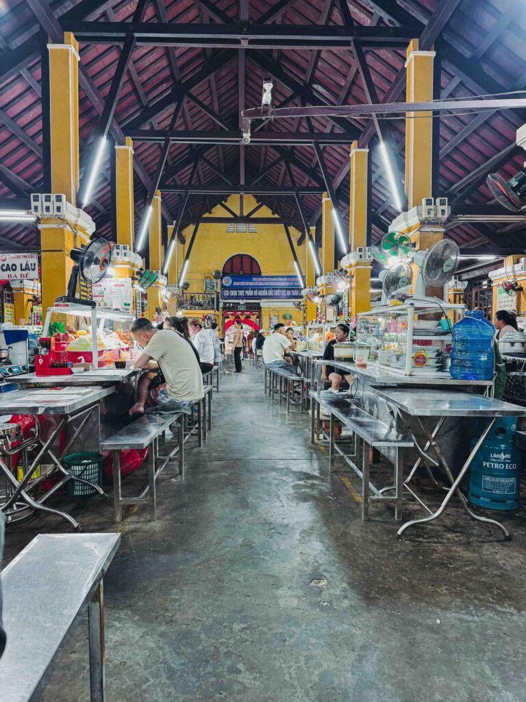 Interior of Hoi An Central Market food hall with yellow pillars dark wooden roof and rows of stainless steel dining benches