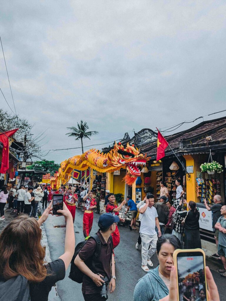 Yellow dragon dance parade winding through crowded Hoi An Old Town street during First Full Moon Festival with Vietnamese flags