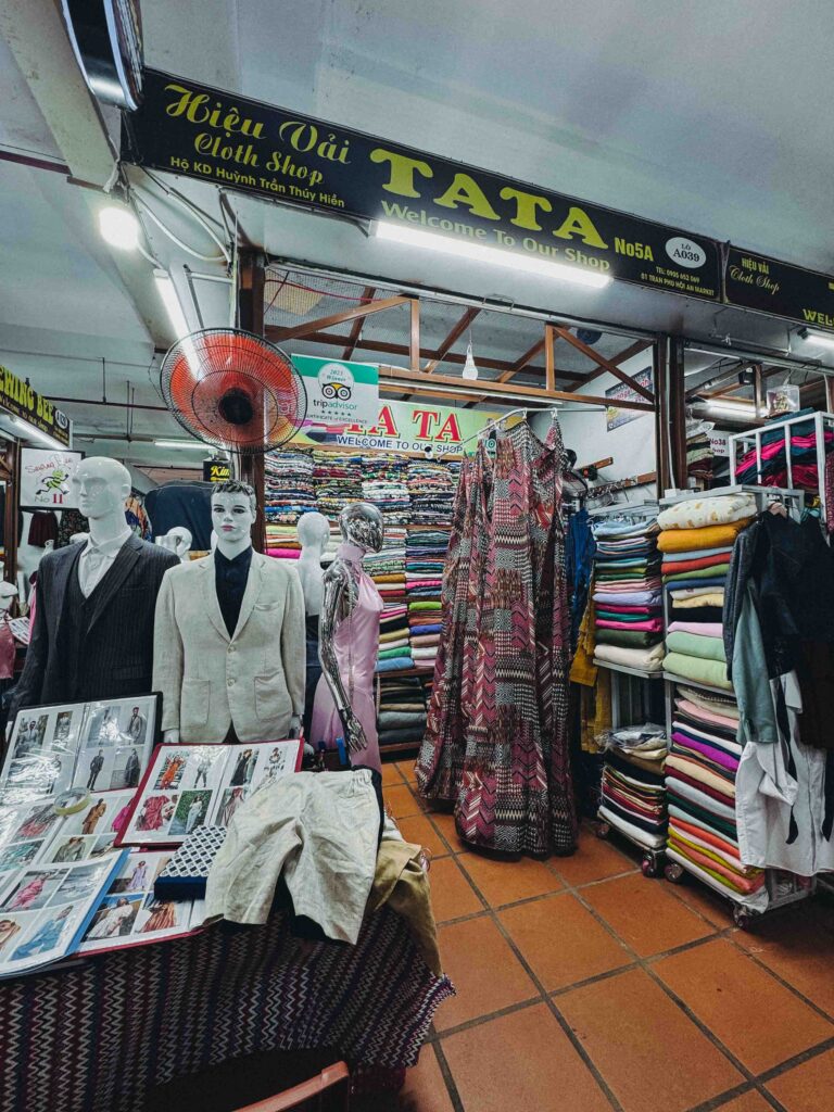 TaTa Tailor cloth shop stall at Hoi An Fabric Market with mannequins in suits colourful fabric rolls and TripAdvisor Certificate of Excellence