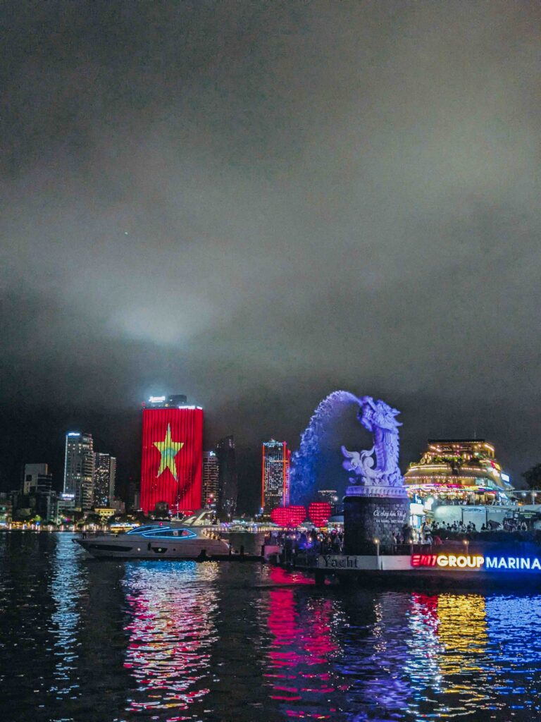 Da Nang city skyline at night reflected in the Han River with Vietnamese flag lit up on a building and dragon sculpture