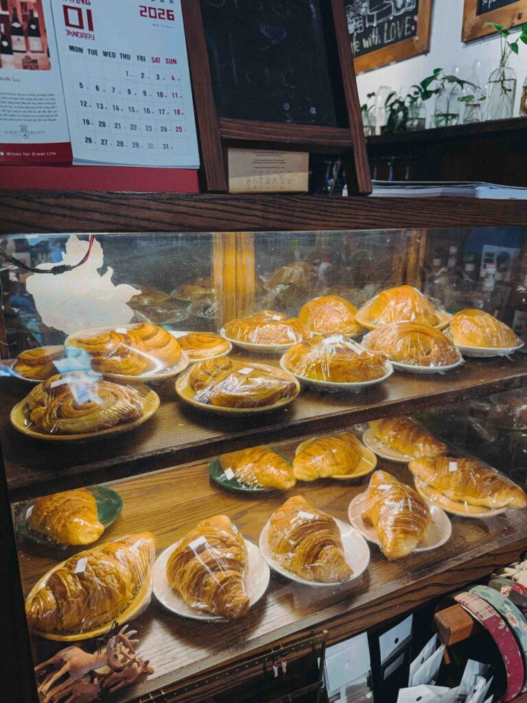 Golden croissants and pastries displayed on plates inside a glass cabinet at Dudu Cafe Hoi An