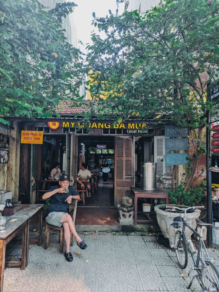 My Quang Ba Mua local food restaurant exterior in Da Nang with man sitting outside eating noodles