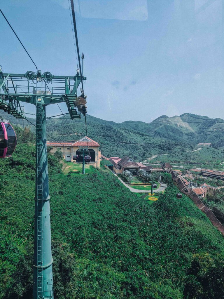 Ba Na Hills cable car ascending over lush green mountains with French Village buildings visible below in Da Nang