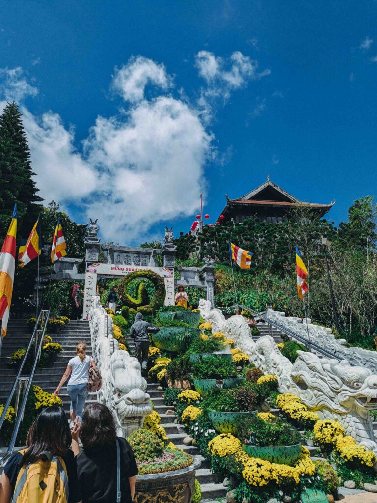 Linh Phong Temple entrance staircase at Ba Na Hills decorated with yellow chrysanthemums dragon statues and Buddhist flags