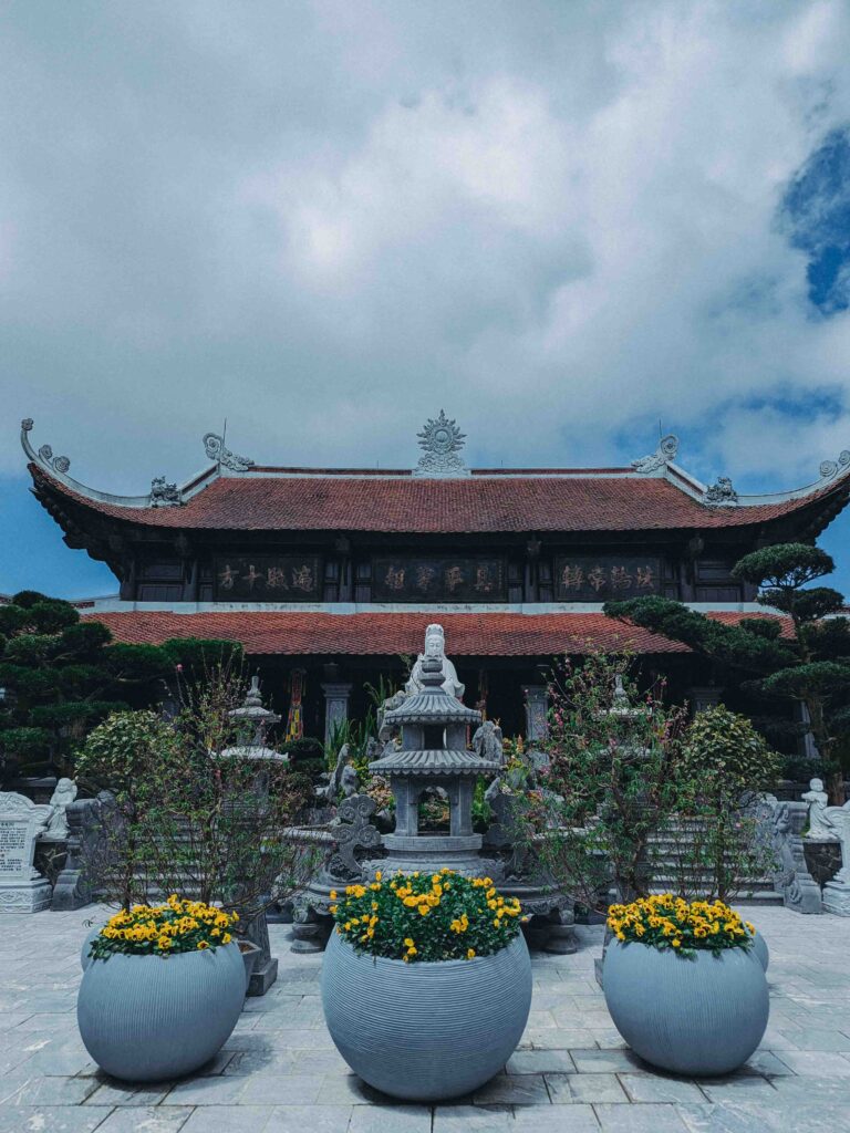 Linh Phong Temple main hall with traditional Vietnamese tiled roof and Guanyin statue surrounded by yellow flowers at Ba Na Hills