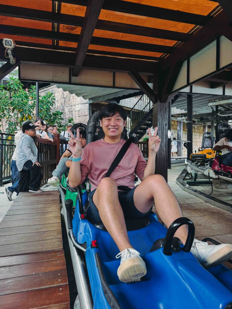 Li Yang smiling and giving peace signs while seated in an Alpine Coaster sled at Ba Na Hills Da Nang