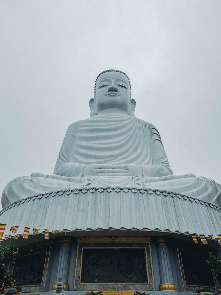 Massive white seated Buddha statue rising above the clouds at Ba Na Hills Da Nang with Buddhist flags at the base
