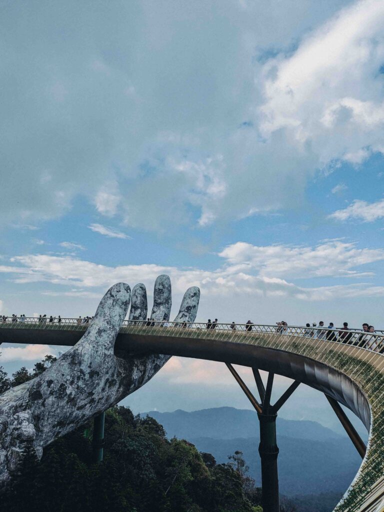 Golden Bridge at Ba Na Hills held by two giant stone hands with tourists walking across and mountain views below